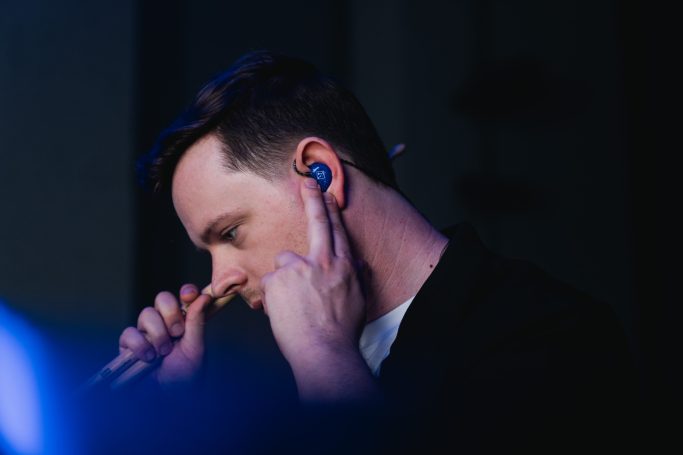 Nahaufnahme eines Musikers beim Einsetzen seiner blauen Hörluchs HL6 In-Ears zur Demonstration der präzisen Passform.