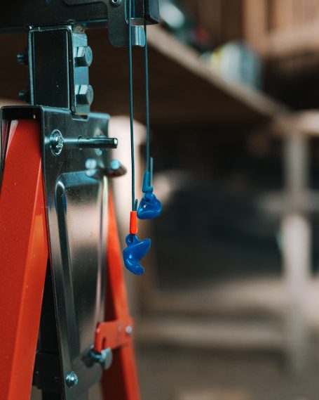 Blauer Hörluchs Gehörschutz mit blauer Verbindungskordel, hängend in einer Werkstatt zur Demonstration der griffbereiten Lagerung.