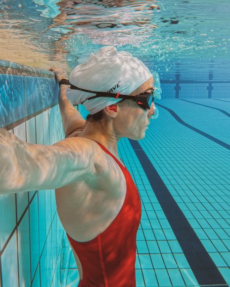Schwimmerin im Pool mit eingesetztem Hörluchs Gehörschutz zur Vermeidung von Wasser im Gehörgang und Entzündungen.