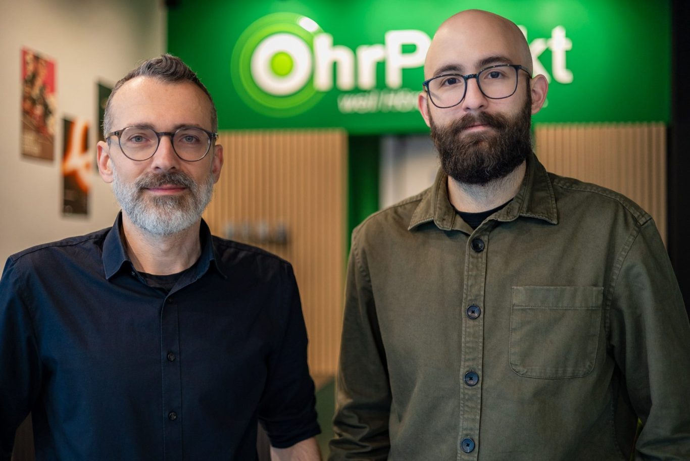 Tobias Hirlinger und Andrés González stehen in ihrem Hörakustikfachgeschäft namens OhrPunkt.