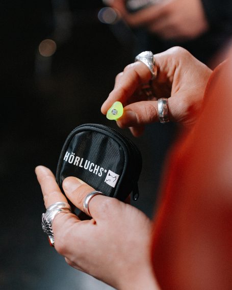 Detailansicht eines Musikgehörschutzes beim Verstauen in die kompakte schwarze Hörluchs-Reißverschlusstasche.