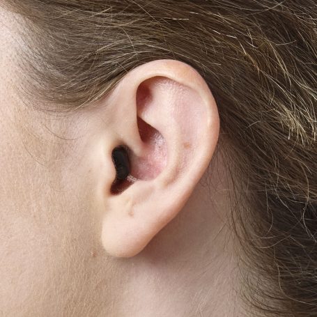 Diskrete Platzierung eines Oticon Zeal Im-Ohr-Hörgeräts (IdO) im Gehörgang zur Demonstration der unauffälligen Bauweise.