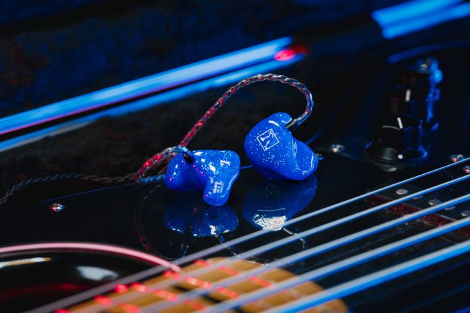 Blaue HL6 Monitoring-Hörer mit Glimmer-Finish, präsentiert auf den Saiten einer Bassgitarre für den Musiker-Bereich.